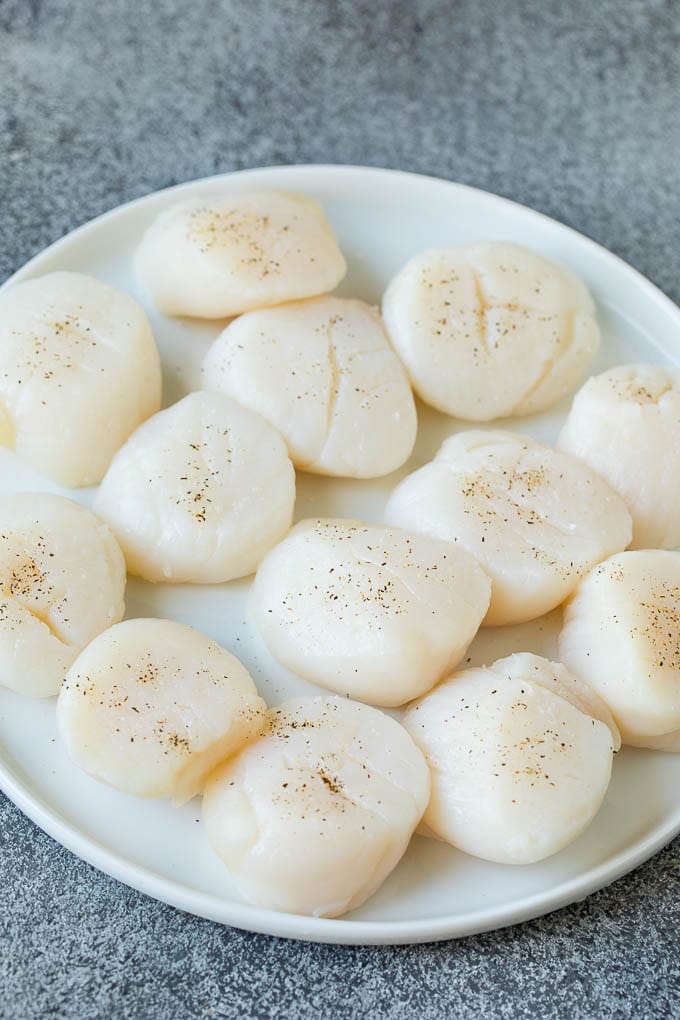 Seared scallops with a garlic and herb butter sauce. An easy and elegant dinner! #seafood #dinner #sadud Raw sea scallops on a plate.