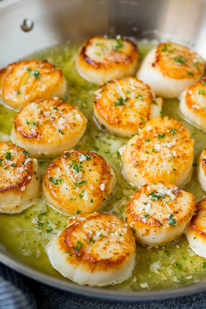 Seared scallops with a garlic and herb butter sauce. An easy and elegant dinner! #seafood #dinner #sadud A pan of scallops in garlic butter.