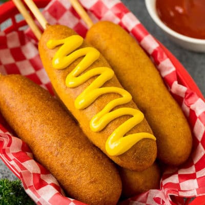 A basket of corn dogs with one topped with mustard.