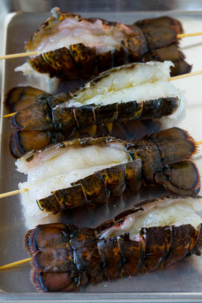 Grilled lobster tail drizzled with garlic butter is an easy and elegant dinner option. #lobster #sadud Raw lobster tails split open with skewers through them.
