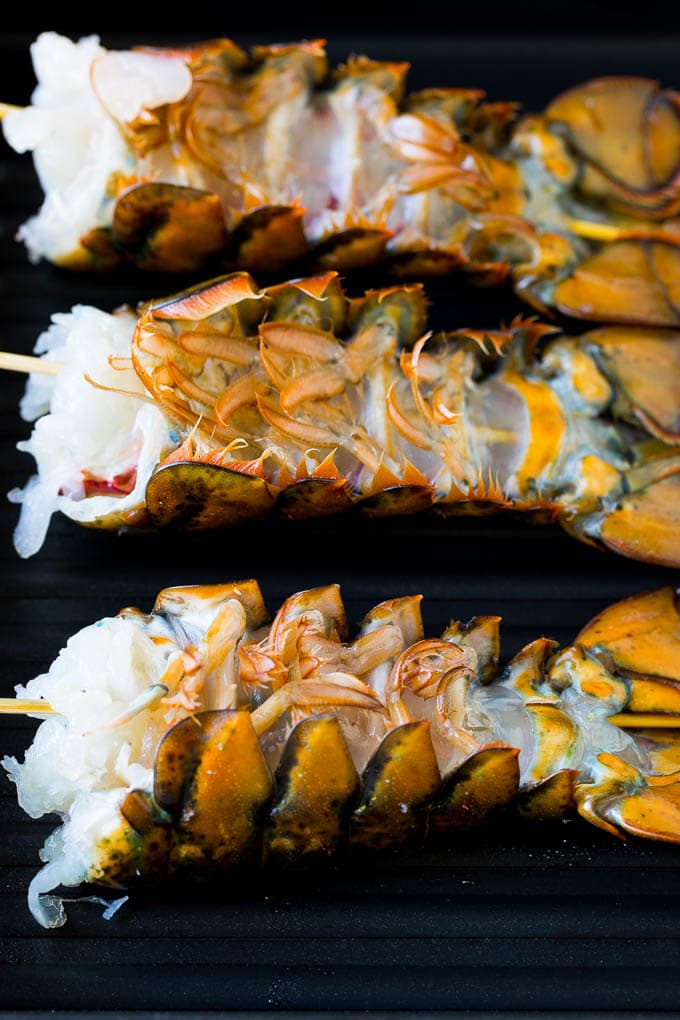 Grilled lobster tail drizzled with garlic butter is an easy and elegant dinner option. #lobster #sadud Lobster tails upside down on a grill pan.