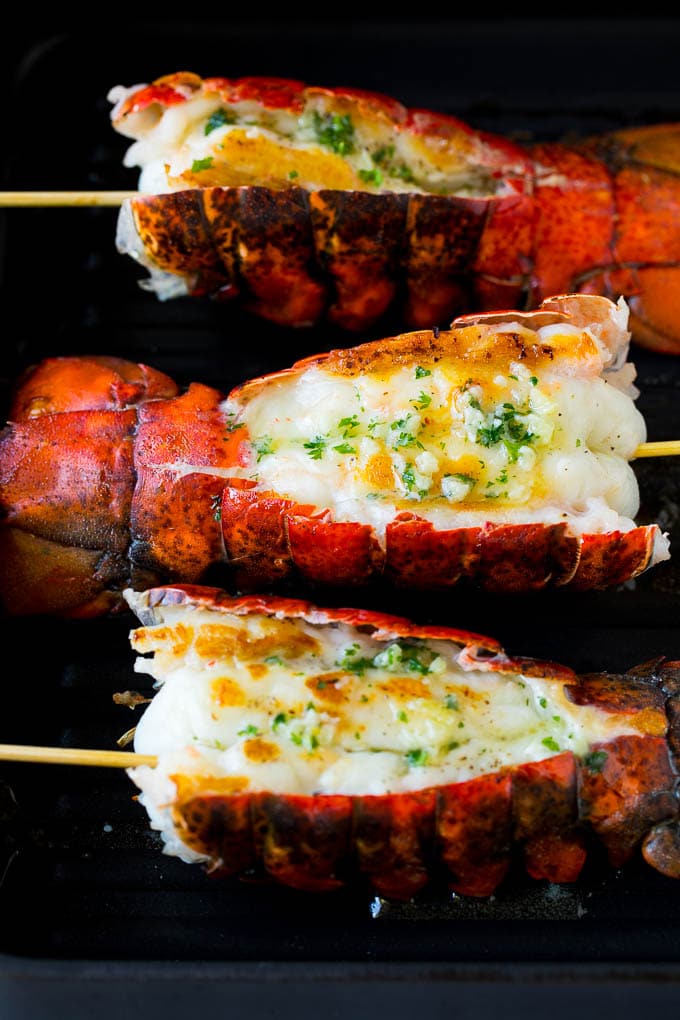 Grilled lobster tail drizzled with garlic butter is an easy and elegant dinner option. #lobster #sadud Cooked lobster tails on a grill pan, brushed with butter.