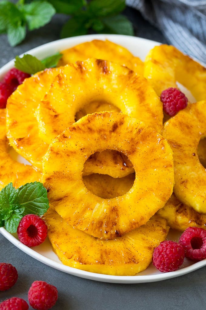 Brown sugar grilled pineapple is a quick and easy side dish or dessert! A plate of grilled pineapple slices garnished with raspberries and mint.