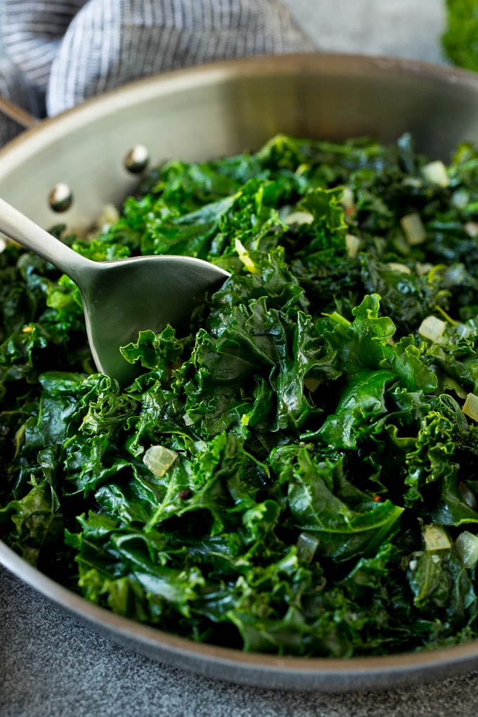 Sauteed kale flavored with olive oil and garlic, a quick and easy side dish! #kale #sadud A pan of sauteed kale with a serving spoon in it.