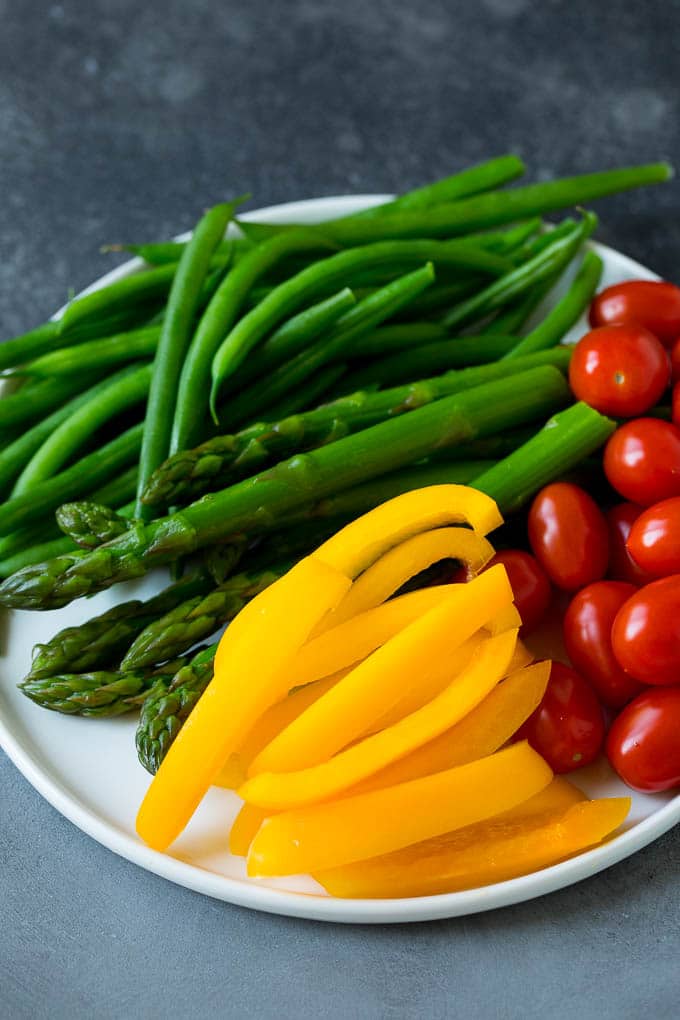 This homemade veggie tray is an assortment of colorful vegetables paired with a variety of flavorful dips. Bell peppers, asparagus, tomatoes and green beans on a plate.