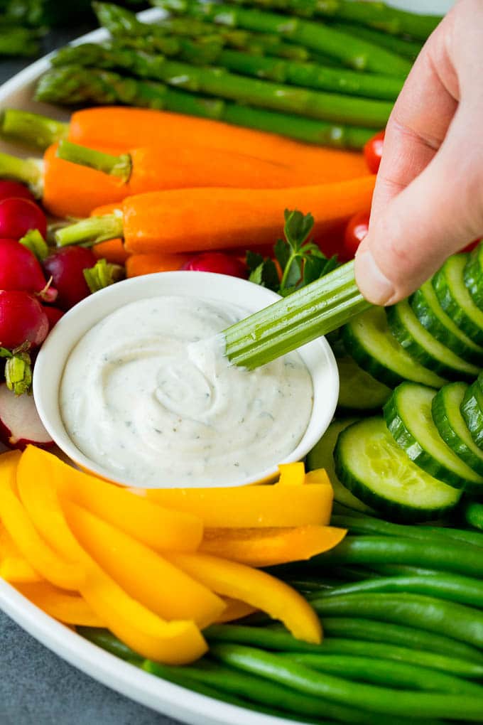 This homemade veggie tray is an assortment of colorful vegetables paired with a variety of flavorful dips. A hand dipping celery into ranch sauce.