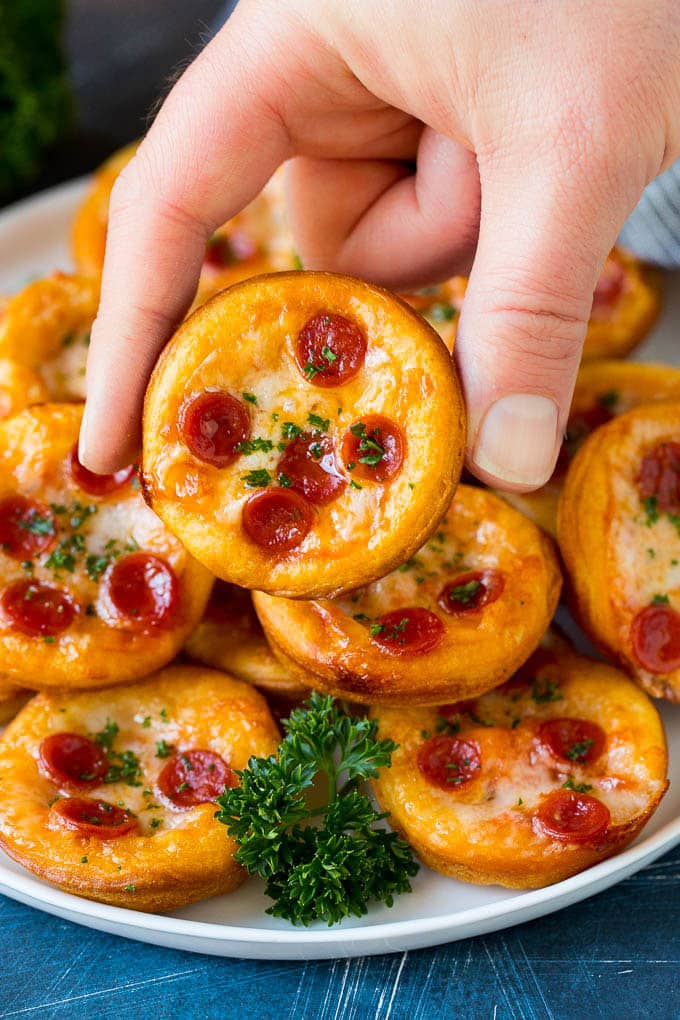 Mini pizzas topped with pepperoni are a fun and easy appetizer option. #pizza #sadud #appetizer A platter of mini pizzas with a hand reaching for one.
