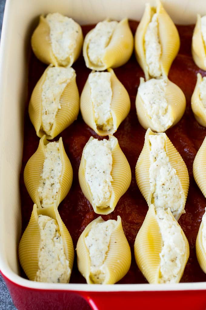 Baked stuffed shells filled with three types of cheese and topped with marinara sauce. #pasta #sadud Pasta filled with cheese on a bed of tomato sauce.