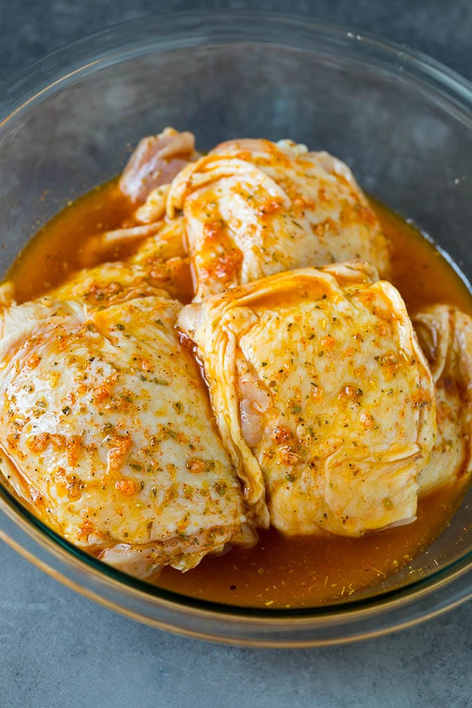 These baked chicken thighs are coated in olive oil, garlic and herbs, then oven roasted until golden brown. A bowl of chicken pieces coated in marinade.