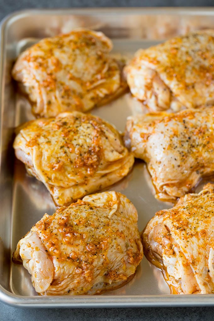 These baked chicken thighs are coated in olive oil, garlic and herbs, then oven roasted until golden brown. Marinated chicken thighs on a sheet pan.