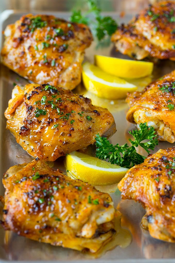 These baked chicken thighs are coated in olive oil, garlic and herbs, then oven roasted until golden brown. A pan of baked chicken thighs garnished with parsley and lemon.
