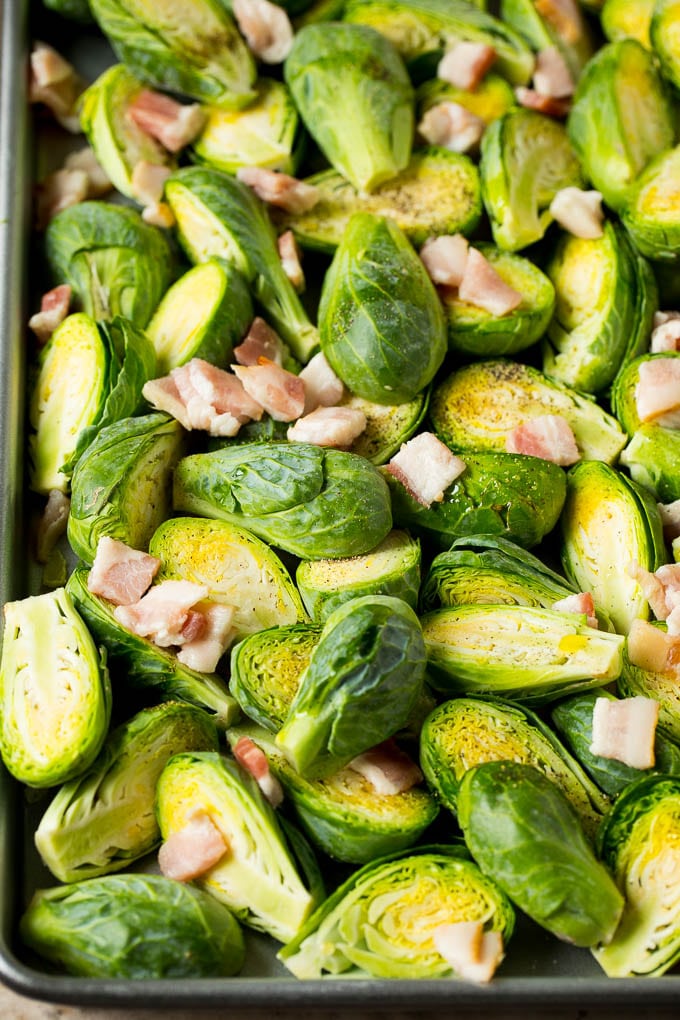 Balsamic brussels sprouts are roasted with bacon, then topped with a drizzle of balsamic glaze. Brussels sprout halves and chopped bacon on a sheet pan.