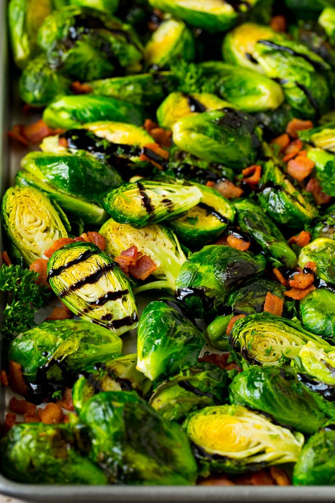 Balsamic brussels sprouts are roasted with bacon, then topped with a drizzle of balsamic glaze. Balsamic brussels sprouts with crispy bacon and parsley on a pan.