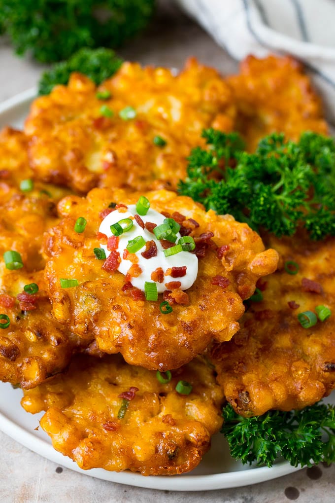 These crispy corn fritters are easy to make and are the perfect appetizer or lighter main course. #corn #sadud A plate of corn fritters garnished with parsley, and topped with sour cream.