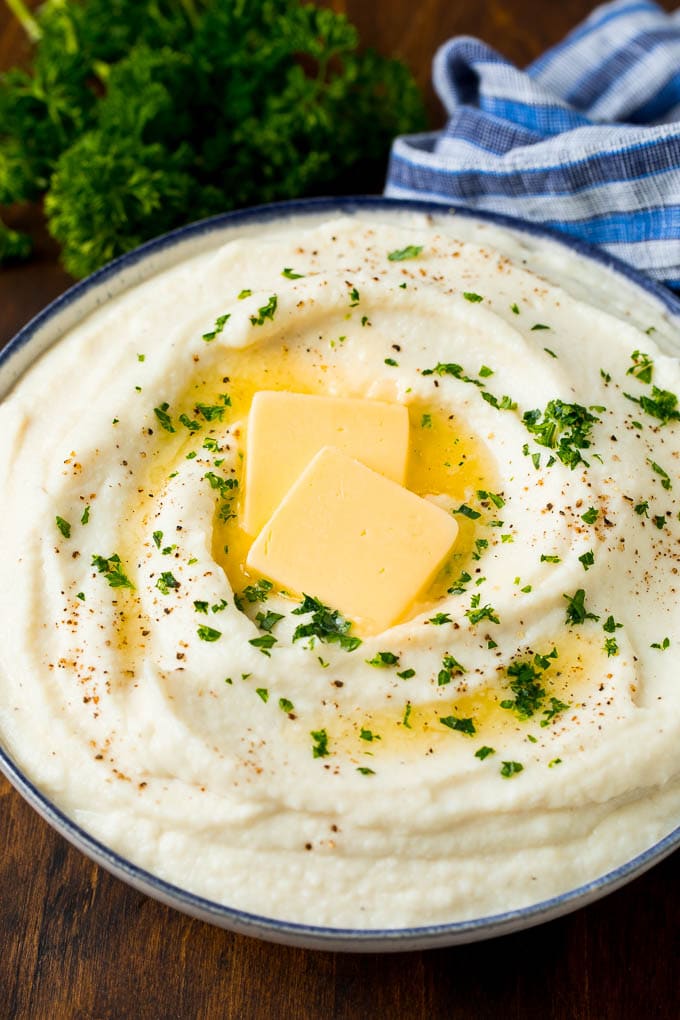 These cauliflower mashed potatoes are mixed with butter, cream and seasonings to make a super delicious side dish that's low in carbohydrates. A bowl of cauliflower mashed potatoes topped with melted butter and parsley.
