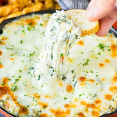 A slice of bread scooping up a serving of spinach artichoke dip.