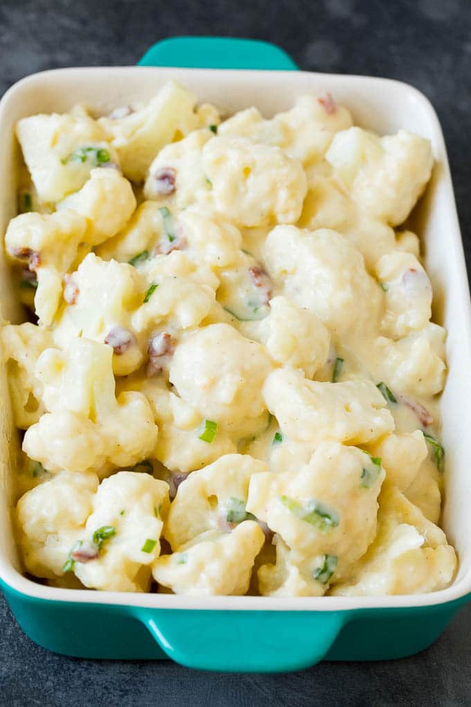 This cauliflower casserole is cooked cauliflower florets tossed in a homemade cheese sauce, then mixed with bacon and green onions and baked to golden brown perfection. Florets tossed with cheese sauce, bacon and green onions in a dish.