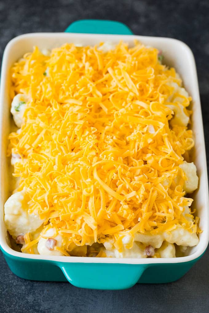 This cauliflower casserole is cooked cauliflower florets tossed in a homemade cheese sauce, then mixed with bacon and green onions and baked to golden brown perfection. Florets in a baking dish, topped with shredded cheese.
