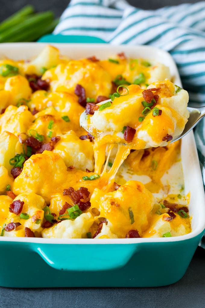 This cauliflower casserole is cooked cauliflower florets tossed in a homemade cheese sauce, then mixed with bacon and green onions and baked to golden brown perfection. A spoon serving up a portion of cauliflower casserole.