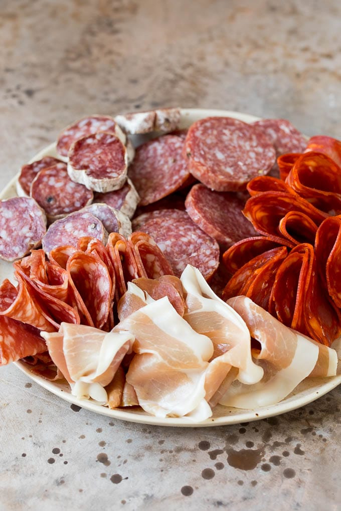 A complete guide on how to put together the best charcuterie board, with a selection of meats, cheeses, crackers, fruit, veggies and other snack foods. Prosciutto and a variety of salami on a plate.