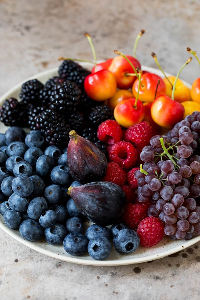 A complete guide on how to put together the best charcuterie board, with a selection of meats, cheeses, crackers, fruit, veggies and other snack foods. A plate of berries, cherries, grapes and figs.