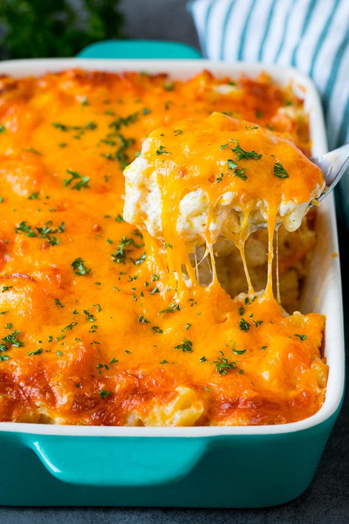These cheesy potatoes are diced potatoes tossed in a creamy blend of sour cream, butter and cheese, then baked to golden brown perfection. A spoon serving up a portion of cheesy potatoes topped with chopped parsley.