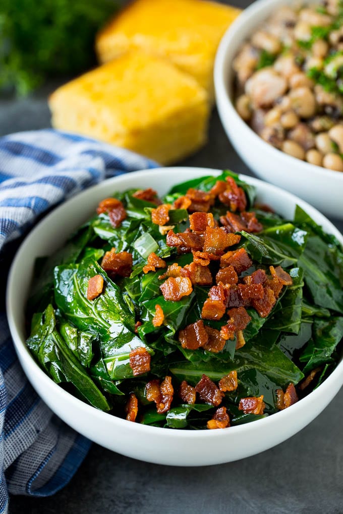 These Southern style collard greens are simmered with bacon and seasonings until tender and flavorful. A bowl of collard greens next to a bowl of black eyed peas and cornbread.