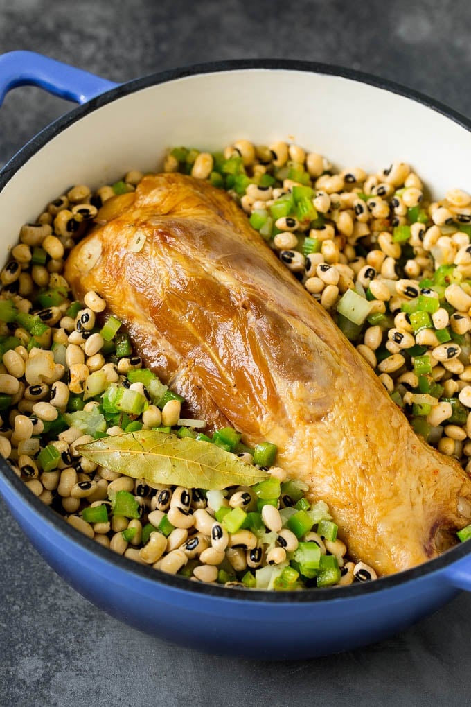This Hoppin' John recipe is black eyed peas simmered with ham and vegetables until tender, then served over rice. A ham shank in a pot of black eyed peas and vegetables.