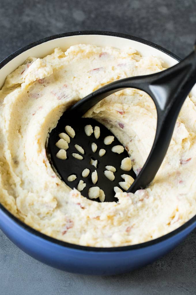 These mashed red potatoes are tender potatoes combined with garlic, butter and seasonings to make a simple yet totally satisfying side dish. A potato masher in a pot of potatoes.