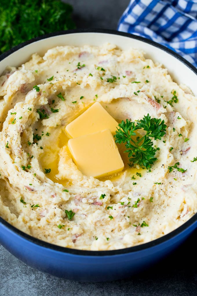 These mashed red potatoes are tender potatoes combined with garlic, butter and seasonings to make a simple yet totally satisfying side dish. A pot of mashed red potatoes garnished with butter and parsley.