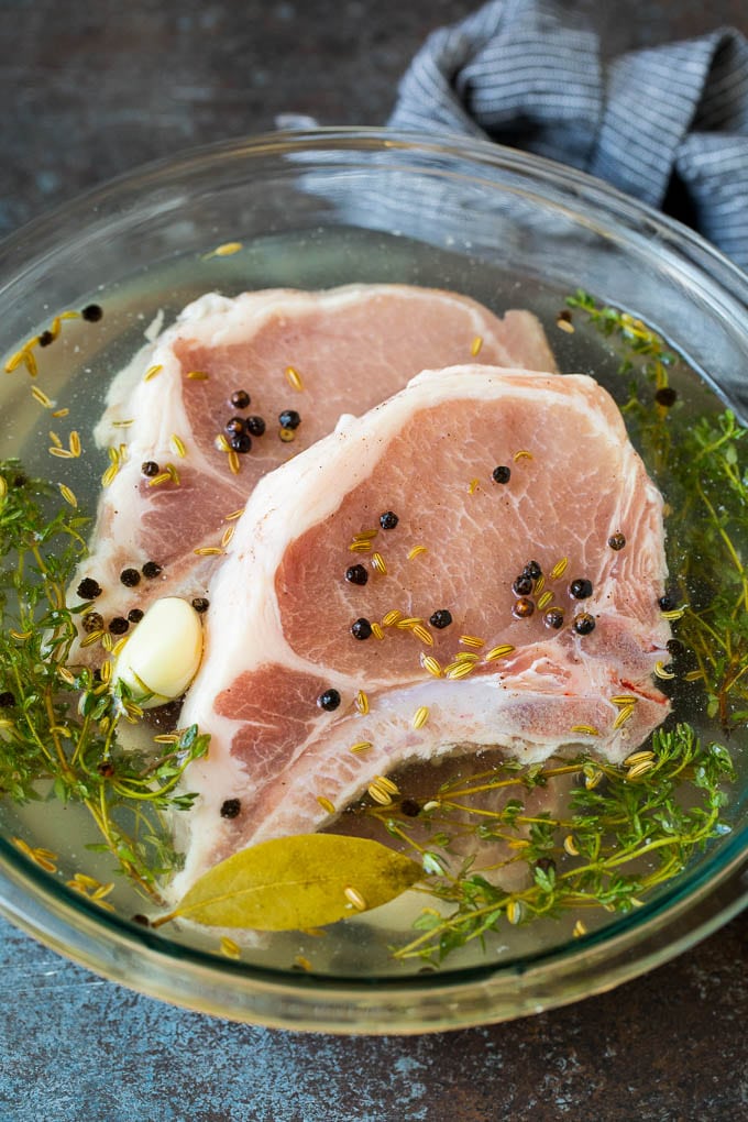 This pork chop brine is a blend of salt, sugar, herbs and spices that infuses the meat with flavor and helps to keep it tender and juicy. A bowl of pork chop brine with raw pork chops in it.