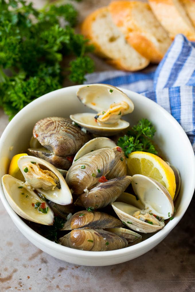 This steamed clams recipe is fresh shellfish cooked with garlic, butter, herbs and lemon. A serving bowl of steamed clams with fresh parsley and sliced bread on the side.