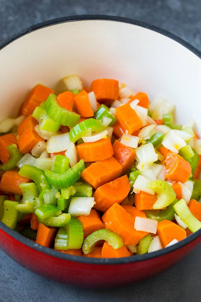 This turkey soup recipe is homemade turkey broth loaded with vegetables, diced turkey and egg noodles. Carrots, celery and onion cooked in a red pot.