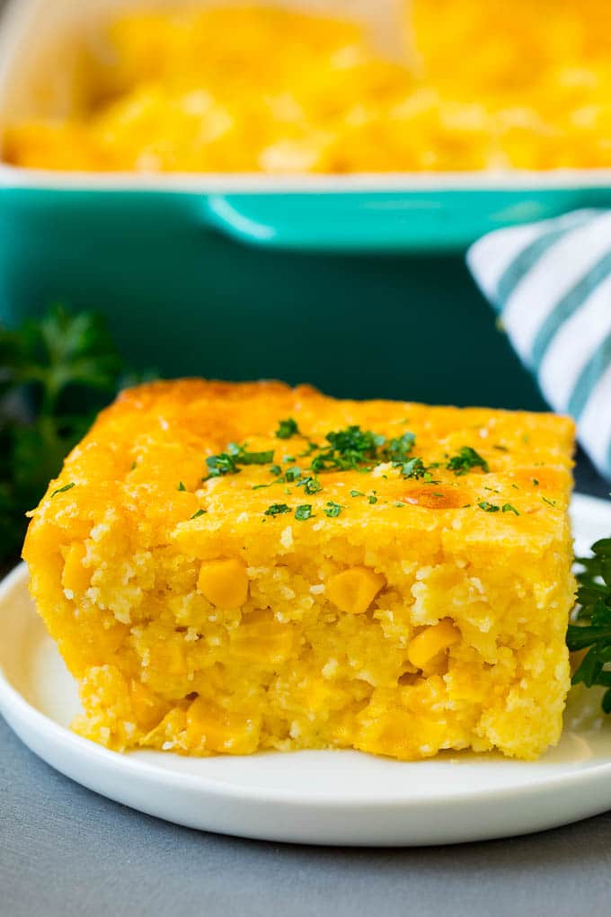 This corn souffle recipe is a flavorful blend of corn kernels, butter, eggs and creamed corn, all baked to light and fluffy perfection. A slice of corn souffle on a plate.