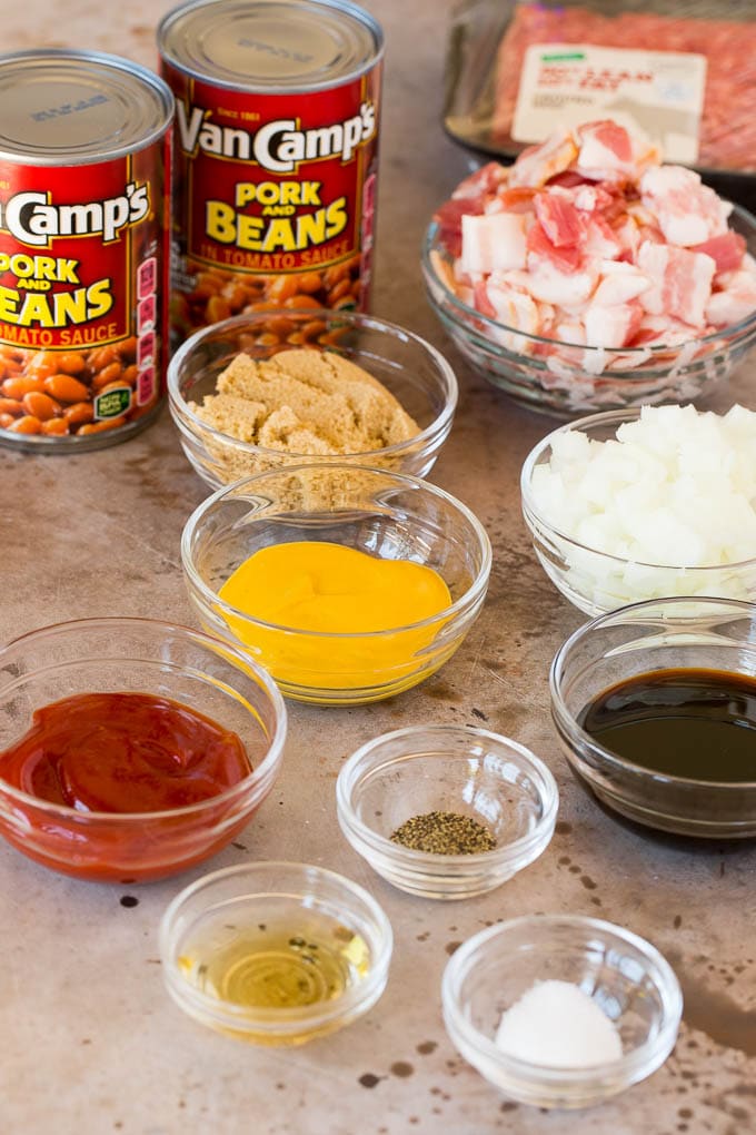 This cowboy beans recipe is made with ground beef and bacon, all baked together in a sweet and savory sauce. Recipe ingredients including bacon, ground beef and bowls of seasonings.