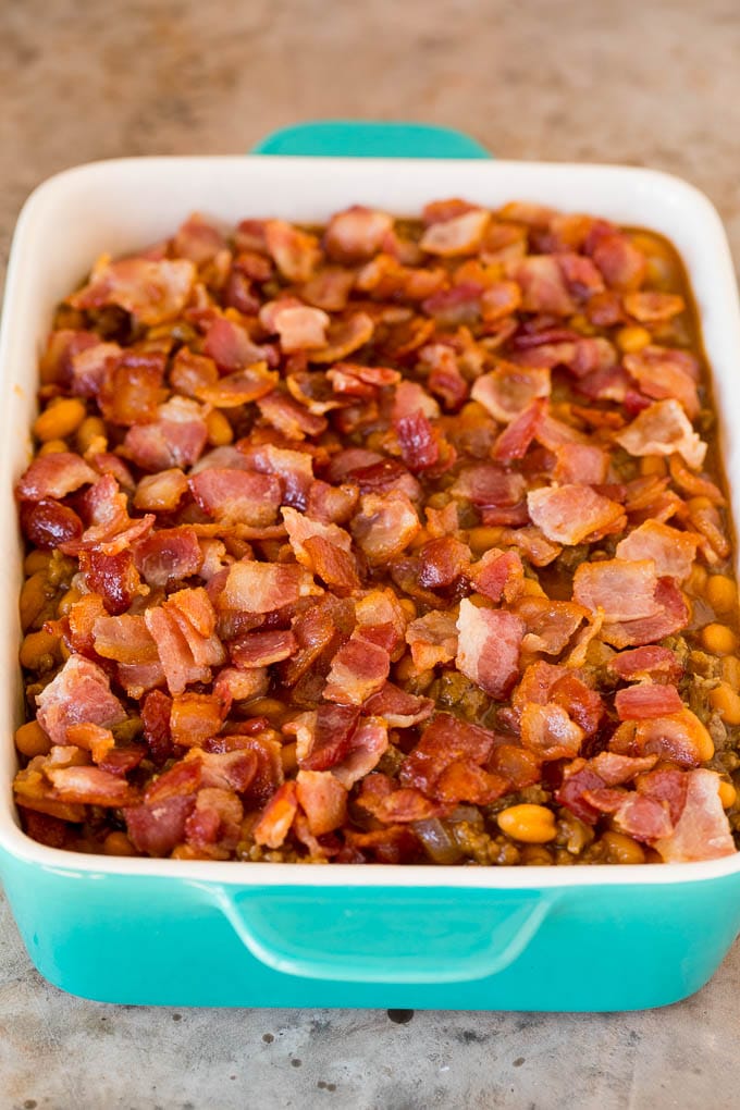 This cowboy beans recipe is made with ground beef and bacon, all baked together in a sweet and savory sauce. A baking dish ready to go into the oven topped with diced bacon.