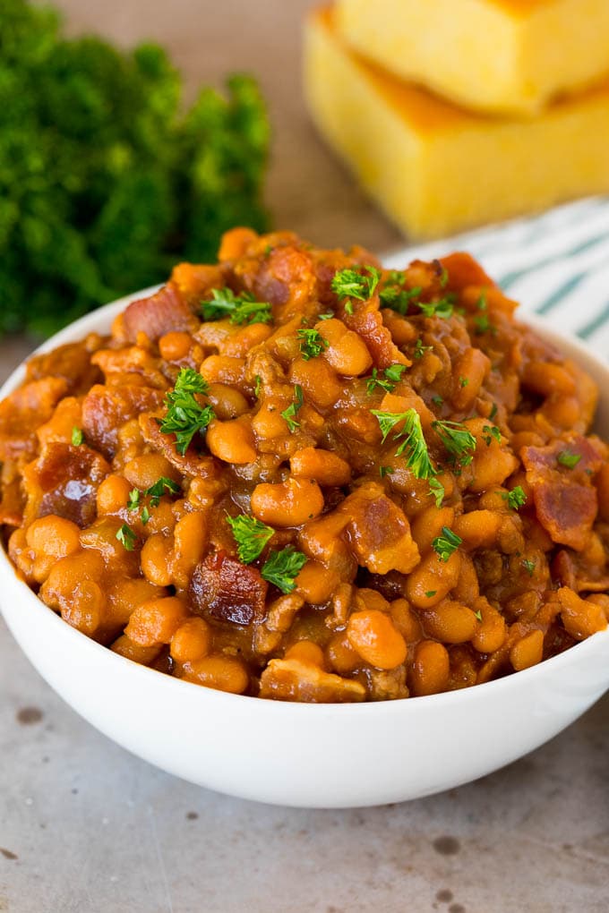 This cowboy beans recipe is made with ground beef and bacon, all baked together in a sweet and savory sauce. A bowl of cowboy beans topped with parsley and served with cornbread.