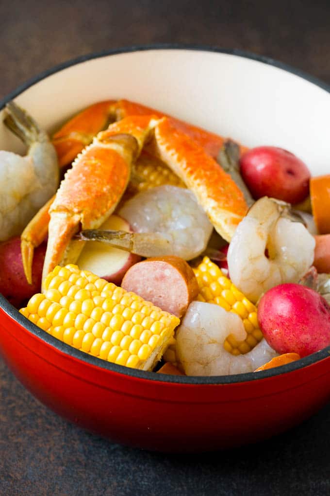 This Low Country Boil is a blend of shrimp, crab, sausage, corn and potatoes, all cooked together to create a hearty dinner. Assorted seafood, sausage and corn in a red pot.