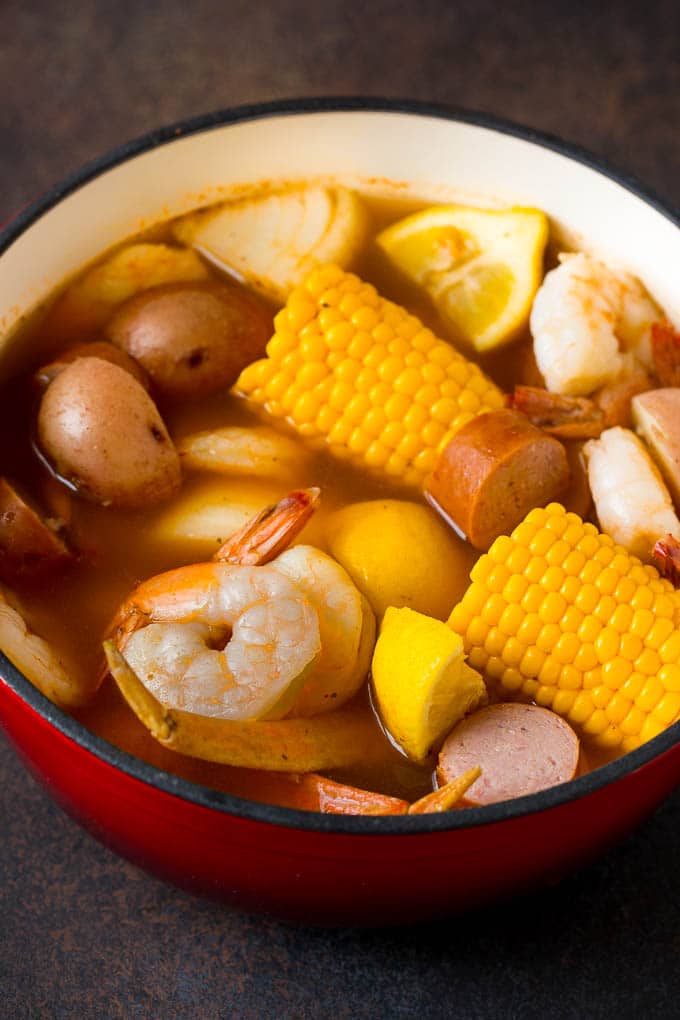 This Low Country Boil is a blend of shrimp, crab, sausage, corn and potatoes, all cooked together to create a hearty dinner. Boiled shrimp, potatoes and corn in a red pot.