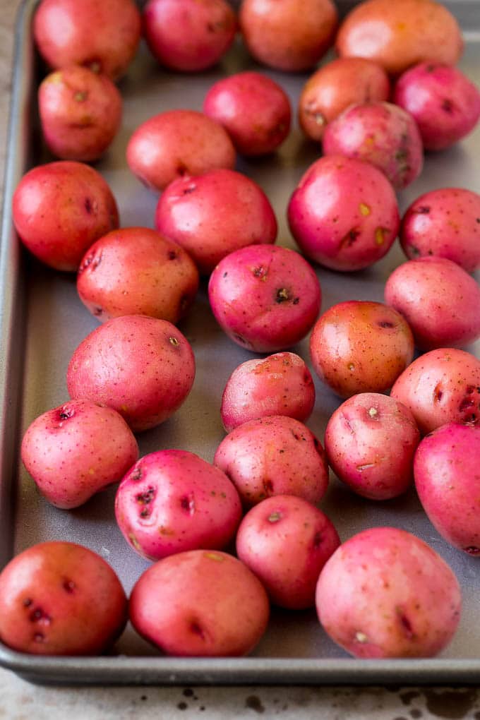 These oven roasted potatoes are baby potatoes coated in olive oil, garlic, herbs and parmesan cheese, then baked until golden brown and crispy. Whole potatoes on a sheet pan.