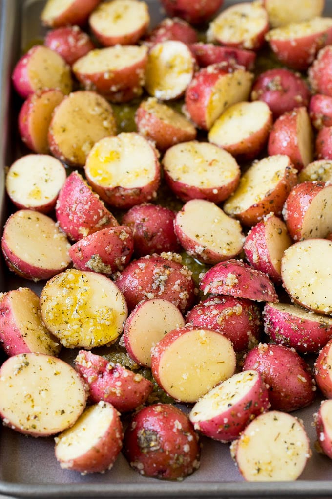 These oven roasted potatoes are baby potatoes coated in olive oil, garlic, herbs and parmesan cheese, then baked until golden brown and crispy. Red potatoes coated in seasonings on a sheet pan.