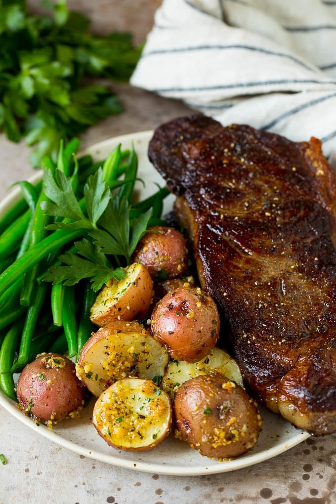 These oven roasted potatoes are baby potatoes coated in olive oil, garlic, herbs and parmesan cheese, then baked until golden brown and crispy. Oven roasted potatoes on a plate with steak and green beans.