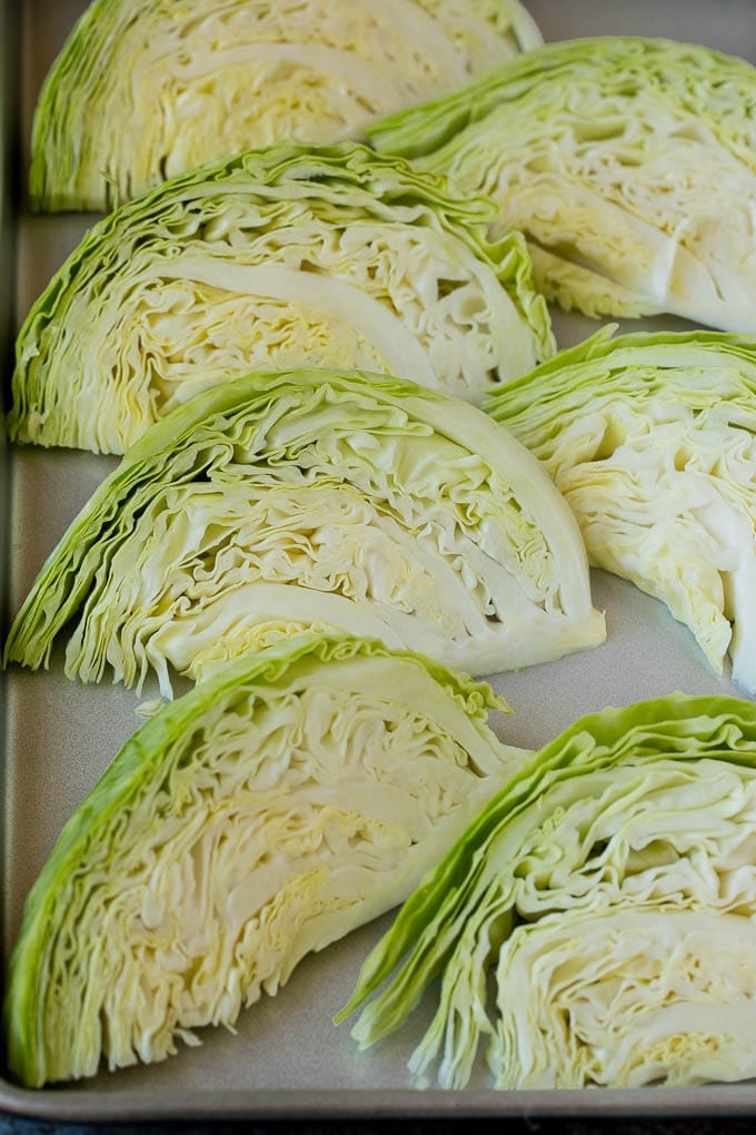This roasted cabbage recipe is wedges of cabbage seasoned with olive oil and spices, then oven baked until tender and browned. Raw cabbage wedges on a pan.