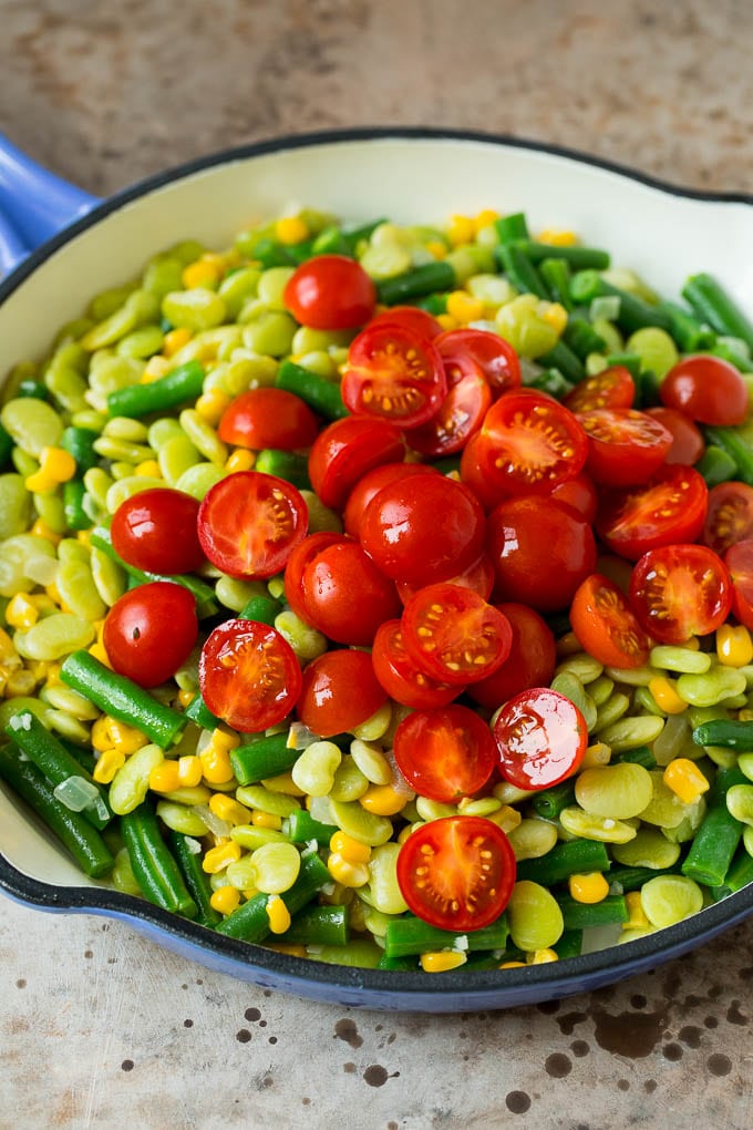 This succotash recipe is a combination of bacon, corn, tomatoes and lima beans, all cooked together to make a colorful and delicious side dish. A pile of cherry tomatoes on top of a mixture of corn and beans.