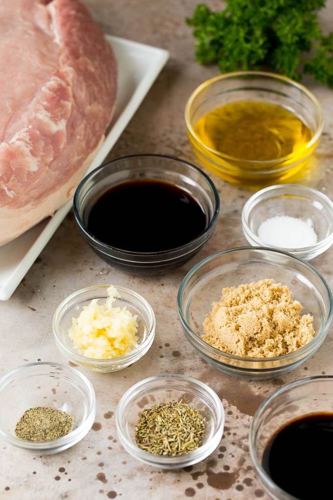 This crock pot pork roast is tender pork loin simmered in a slow cooker in a rich and flavorful gravy. Bowls of herbs, spices and seasonings next to a piece of pork.
