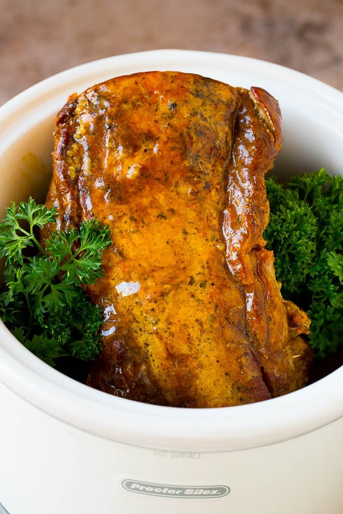 This crock pot pork roast is tender pork loin simmered in a slow cooker in a rich and flavorful gravy. Crock pot pork roast inside a slow coker with gravy, garnished with parsley.