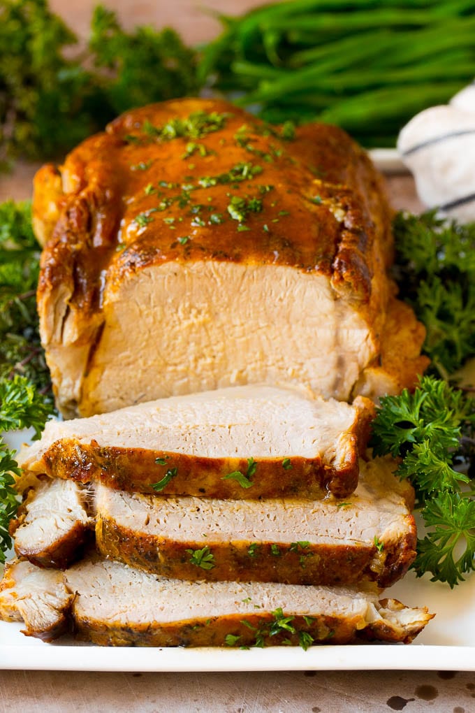 This crock pot pork roast is tender pork loin simmered in a slow cooker in a rich and flavorful gravy. Crock pot pork roast sliced on a serving plate, garnished with herbs.