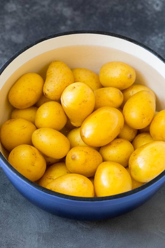 These smashed potatoes are baby potatoes that are boiled until tender, then smashed flat, topped with garlic and herb butter, and roasted until crispy and browned. Baby potatoes in a pot of water.