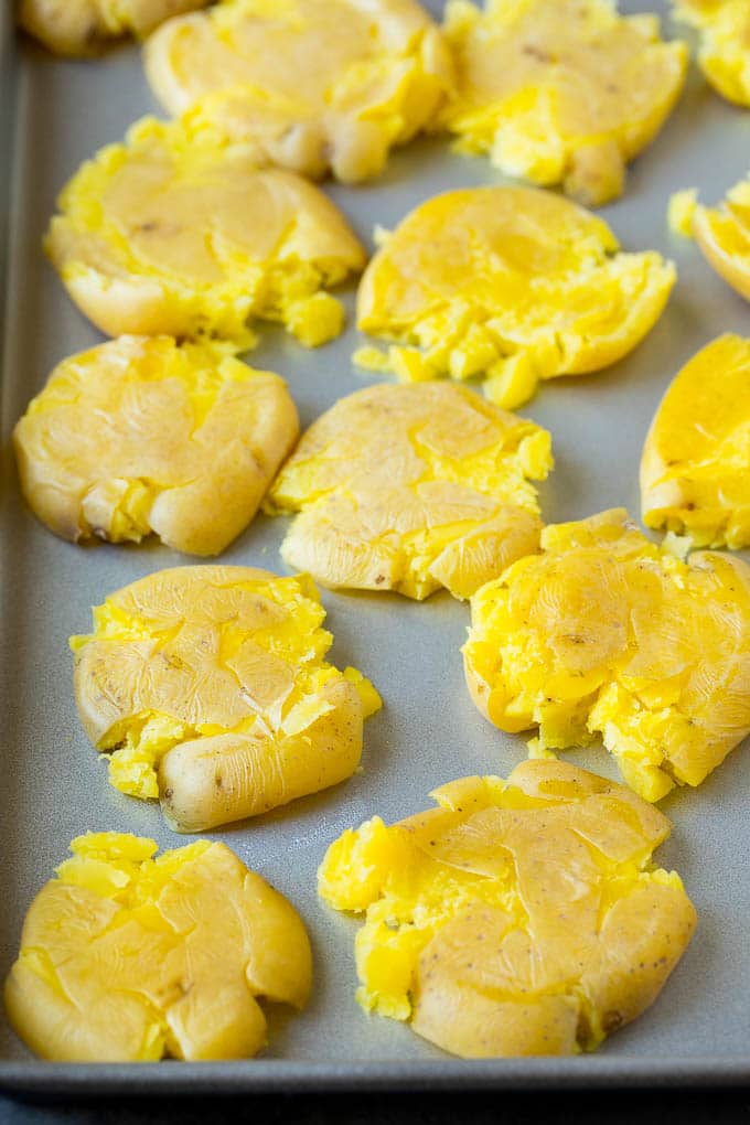These smashed potatoes are baby potatoes that are boiled until tender, then smashed flat, topped with garlic and herb butter, and roasted until crispy and browned. Flattened potatoes on a sheet pan.