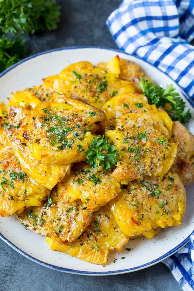 These smashed potatoes are baby potatoes that are boiled until tender, then smashed flat, topped with garlic and herb butter, and roasted until crispy and browned. A serving plate of smashed potatoes garnished with parsley.